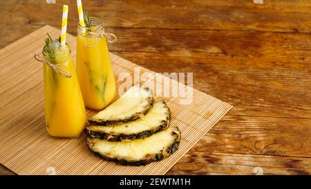 Frisch zubereitetes Ananassaft mit Eis in einem kleinen Glas Flasche auf Holzhintergrund Stockfoto