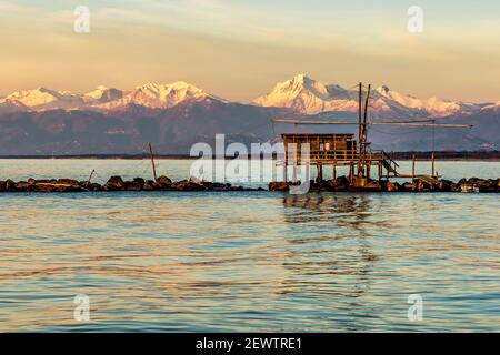 Baumhüttenangeln bei Sonnenuntergang, gegen die mit Schnee bedeckten Alpen, Marina di Pisa, Toskana, Italien Stockfoto