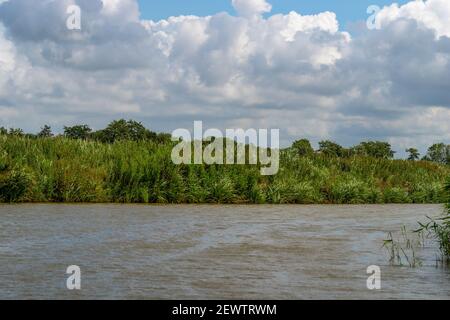 Blick über einen Kanal mit Schilf und dramatische Wolken im blauen Himmel in Friesland, Niedersachsen, Deutschland Stockfoto