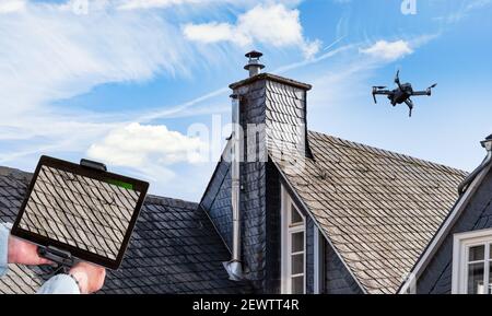 Drohne in der Luft, die das Dach über dem Haus inspiziert. Nahaufnahme von Drohne und Dach. Stockfoto