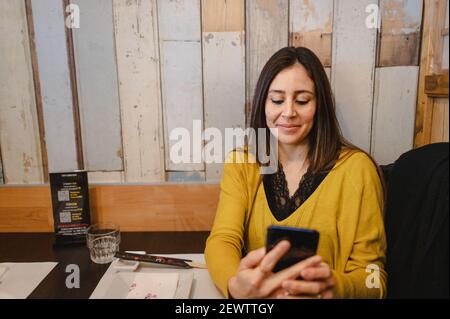 Ein Porträt einer jungen glücklichen Frau, die sie anlächelt Telefon in einem chinesischen Restaurant mit Holzwänden Stockfoto
