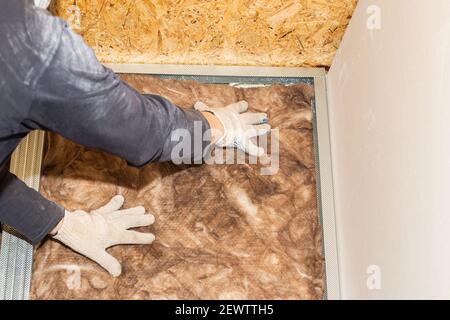 Der Arbeiter fügt Mineralwolle an die Wände für weitere Gipskartonverkleidungen. Wärmedämmung und Schalldämmung des Gehäuses. Renovierung des Hauses. Stockfoto