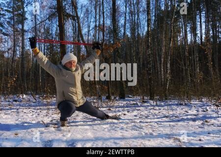 Ältere Frau, die beim Nordic Walking mit Stöcken trainiert Winterwald Stockfoto