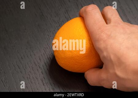 Männliche Hand nimmt eine Orange auf einem schwarzen Holz Nahaufnahme im Hintergrund mit Kopierbereich Stockfoto