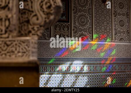 Buntes Licht aus einem Buntglasfenster, das auf die aufwändigen Wandentwürfe einer Moschee in der Medina von Fes, Marokko, gegossen wird Stockfoto