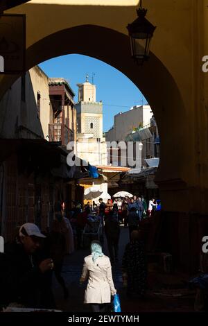 Eine Frau geht in den Schatten unter einem mittelalterlichen Tor mit Minarett im Hintergrund, Fes, Marokko Stockfoto