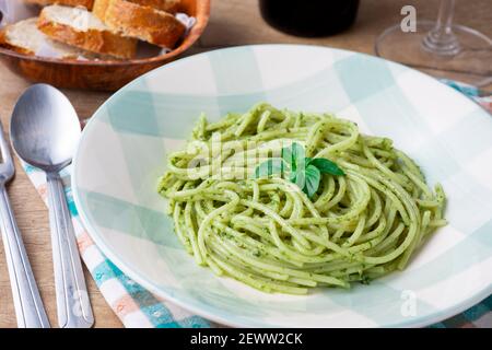 Spaghetti mit Pesto auf einem weißen und grünen Teller mit Brot und einem Glas Wein. Stockfoto
