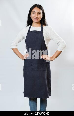 Schürze Mockup - hispanische Frau trägt blaue Schürze - Junge arbeitende Frau lächelnd. Junge Köchin Stockfoto