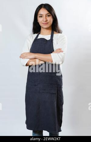 Hispanische Unternehmerin Frau mit blauen Schürze - zuversichtlich und glücklich Arbeitende Frau mit gekreuzten Armen - Junge Köchin Stockfoto