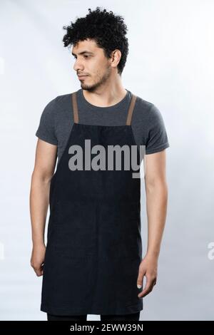 Schwarze Schürze Mockup - Hispanic Junger Mann Trägt Schürze Lächelnd Auf weißem Hintergrund - junger Arbeiter Stockfoto