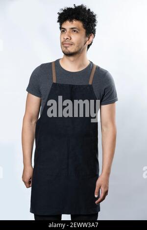 Schwarze Schürze Mockup - Hispanic Junger Mann Trägt Schürze Lächelnd Auf weißem Hintergrund - junger Arbeiter Stockfoto