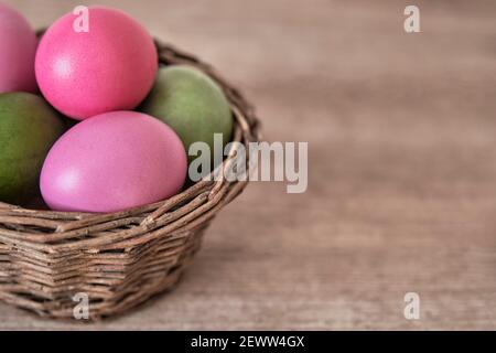 Bunte Hühnereier mit natürlichen Lebensmittelfarben in einem Korb von Weidenzweigen auf einem hölzernen Hintergrund gemalt. Nahaufnahme. Osterfeiertagskonzept Stockfoto