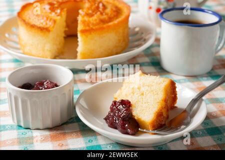 Kuchen, Kuchen in Scheiben, Beerenmarmelade und eine Tasse Kaffee über karierten Textilien. Home Frühstücksszene. Stockfoto