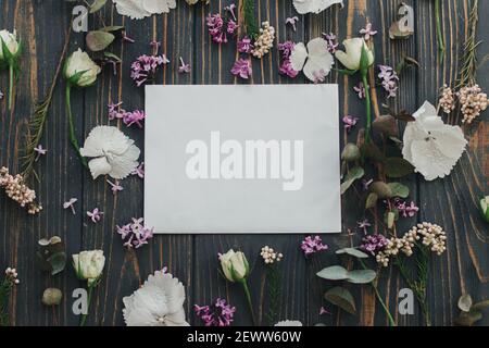 Grußkarte und Flieder, Eukalyptus, Hortensien, Rosenblätter auf dunklem Holzhintergrund flach legen. Grußkartenvorlage mit Blumenmuster. Blühende Frühlingsblume Stockfoto