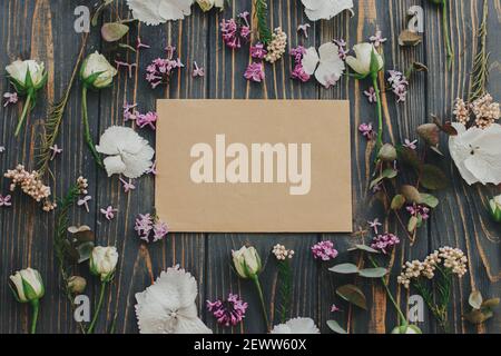 Grußkartenvorlage mit Blumenmuster. Grußkarte und Flieder, Eukalyptus, Hortensien, Rosenblätter auf dunklem Holzhintergrund flach legen. Blühende Frühlingsblume Stockfoto