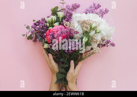 Hände halten moderne frische Bouquet auf hellen rosa Hintergrund flach legen. Stilvolle bunte Grußkarte mit Pfingstrose, Flieder, Eukalyptus, Hortensien Blumen Stockfoto