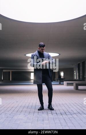 Ein gutaussehender Geschäftsmann, der mit einem Laptop auf seine Uhr schaut. Stockfoto