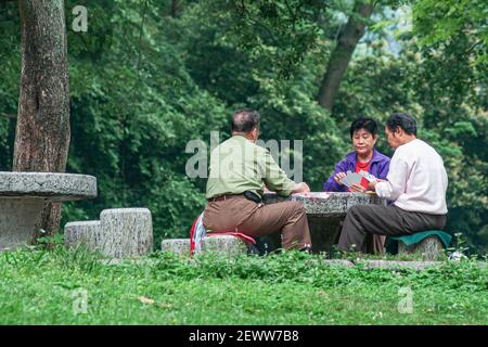 Guilin, China - 11. Mai 2010: Seven Star Park. Frau und 2 Männer spielen Karten auf Steintisch umgeben von grünem Laub. Stockfoto