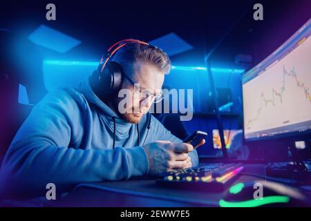 Junge männliche Trader Aktienmarkt Broker Analyse Grafiken Computer-Bildschirm verwendet Telefon, Neon-Farbe. Stockfoto
