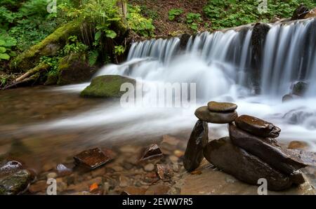Balancierte gestapelte Steine neben Wasserfall am Bergfluss Stockfoto