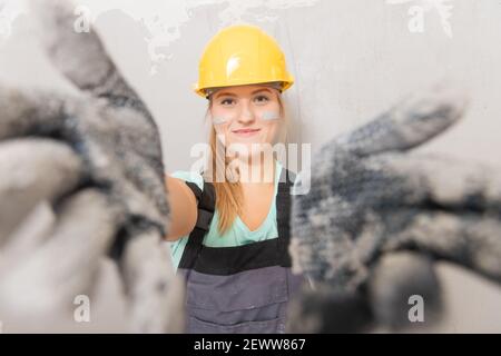Bauherrin Frau in gelbem Helm auf dem Hintergrund der grauen Wand, Gesicht in Gips. Stockfoto