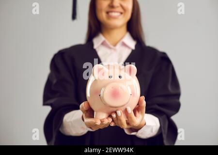 Nahaufnahme eines Sparschweines in den Händen einer Schülerin auf grauem Hintergrund. Bildungsfonds. Stockfoto