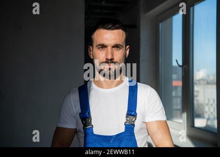 Ein Baumeister in einem blauen Overall steht im Schatten Stockfoto