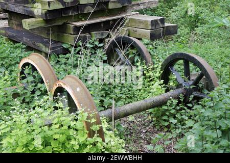 Heritage Eisenbahnlinie Outdoor-Shop mit zwei Sets von rostigen Rädern und einem Stapel von hölzernen Schwellen mit Brennesseln und Knoblauch Senf Pflanzen. Stockfoto