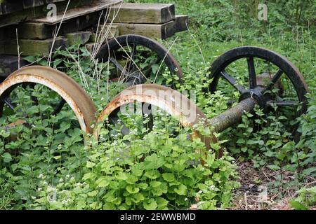 Heritage Eisenbahnlinie Outdoor-Shop mit zwei Sets von rostigen Rädern und einem Stapel von hölzernen Schwellen mit Brennesseln und Knoblauch Senf Pflanzen. Stockfoto