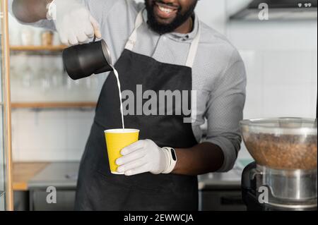 Nahaufnahme Biracial Barista Vorbereitung Latte Kaffee zu gehen, ein multirassischer Kellner gießt Milch in Papiertasse, zum Mitnehmen heiße Getränke bestellen, zugeschnittenes Bild Stockfoto