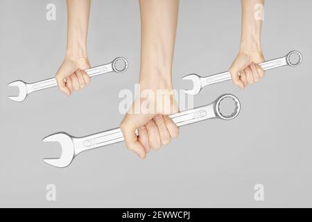 Drei Schraubenschlüssel in den Händen der Frauen. Hände halten einen Schraubenschlüssel auf einem grauen Hintergrund. Kombinationsschlüssel. Großer Chrom-Vanadium-Schraubenschlüssel in der Hand. Frauen Stockfoto