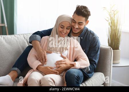 Glücklich Schwanger Muslim Paar Entspannen Auf Couch Zu Hause Stockfoto