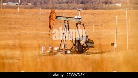 Rusty Gas - Öl pumpjack in einem orange winter Feld voll von elektrischen Polen mit unscharfen Gras im Vordergrund. Stockfoto