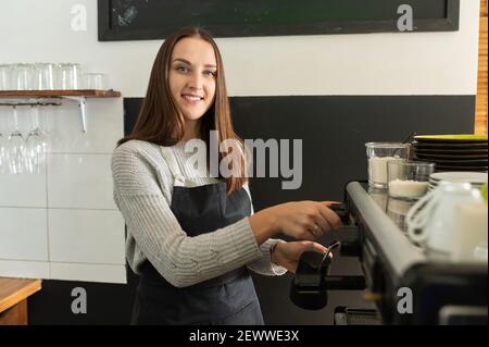 Weibliche Barista trägt Schürze, die Kaffee in einem Café zubereitet, professionelle Kaffeebrau. Inhaber des kleinen Unternehmens, Kellnerin Stockfoto