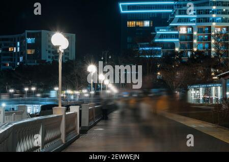 Menschen in verschwommener Bewegung auf der beleuchteten nächtlichen Stadtstraße. Stockfoto