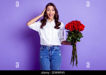 Foto von stauned fröhlich Dame halten roten Rosen Palmkopf Tragen weiße Hemd isoliert violette Farbe Hintergrund Stockfoto