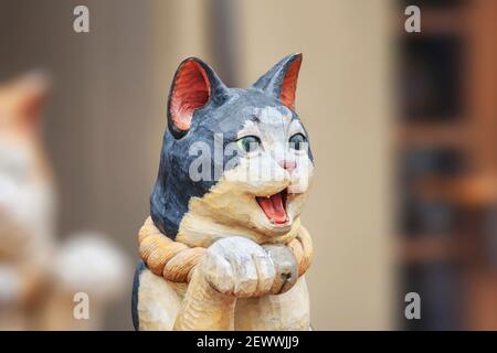 tokio, japan - februar 28 2021: Nahaufnahme einer Holzskulptur, die eine niedliche japanische Maneki-Neko-Katze mit offenem Mund und einer Pfote in einer Be zeigt Stockfoto