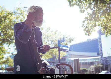 afroamerikanischer älterer Mann sitzt auf dem Fahrrad in der Straße Putting Mit Kopfhörern Stockfoto