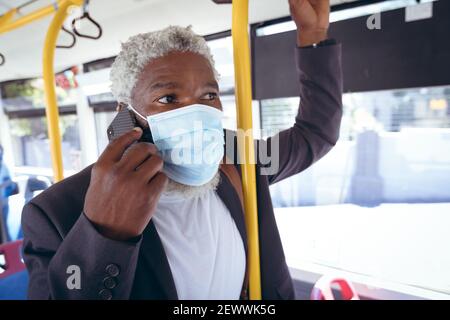 afroamerikanischer älterer Mann mit Gesichtsmaske auf Bus stehend Sprechen auf dem Smartphone Stockfoto