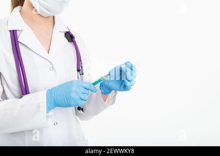 Eine junge Krankenschwester in einer Maske öffnet eine Spritze auf weißem Hintergrund in einem weißen Mantel, um eine Impfung, eine Injektion zu machen. Das Konzept der Impfung und Stockfoto