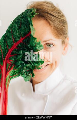 Frau Chefin hält bunte schweizer Mangold Blatt vor Ihr Gesicht Stockfoto