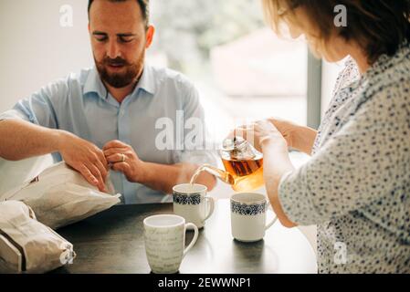 Pärchen beim Frühstück mit Tee. Mann öffnet Beutel mit frischem Gebäck Stockfoto