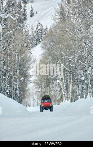 SUV mit Weihnachtsbaum auf dem Dach fährt verschneiten Berg hinunter Forststraße Stockfoto