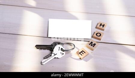 Modell, leere Visitenkarte und Heimschild mit Schlüsseln auf Holzhintergrund. Immobilienkonzept. Draufsicht. Stockfoto