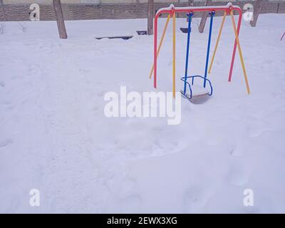 Kinderschaukel im Schnee. Der Spielplatz ist mit Schnee bedeckt. Leerer Spielplatz. Stockfoto
