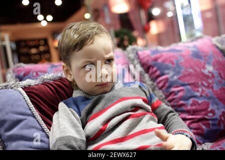 Verärgert Kind sitzt auf einem roten Sofa Stockfoto