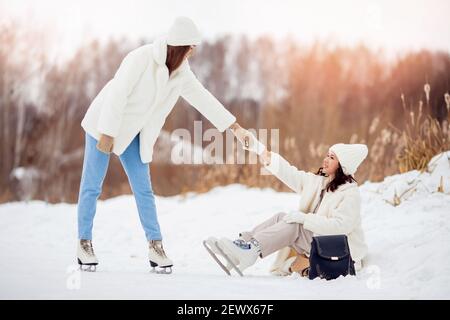 Junges Mädchen hilft ihrem Freund auf Eis Winterbahn Schlittschuh. Stockfoto