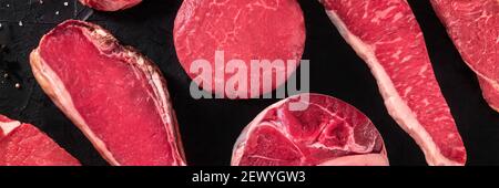 Rotes Fleischpanorama. Rohe Rindersteaks, von oben auf schwarz geschossen Stockfoto