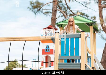 Spiele für Kinder. Ein kleines Mädchen macht Gesichter, während sie auf einem hölzernen Spielturm steht. Stockfoto