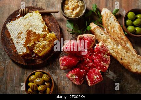 Von oben die Hälfte des Granatapfels und der süßen Wabe auf gelegt Rustikaler Holztisch neben Oliven und Baguette Toast mit Hummus Stockfoto